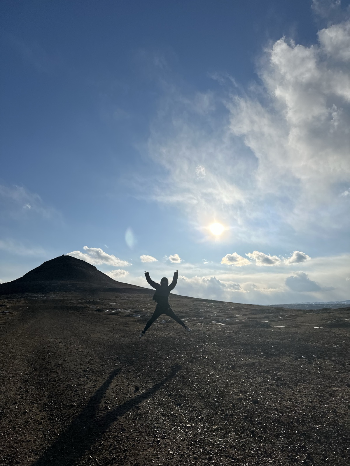 一名同行者在火山与低太阳之间跃起,身影落在黑色地面上