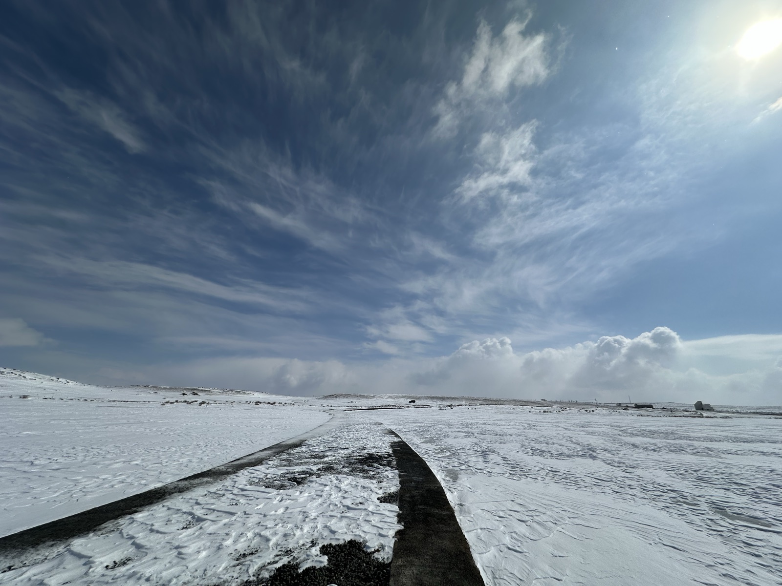 积雪覆盖的原野中,一条深色道路伸向云层下的远方